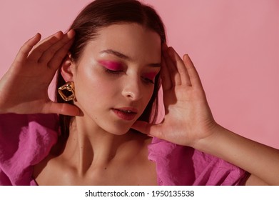 Close up beauty portrait of young beautiful woman with pink, fuchsia color eyeshadow makeup, flawless clean skin, wearing elegant golden earrings, pink blouse. Spring, summer fashion trend - Shutterstock ID 1950135538