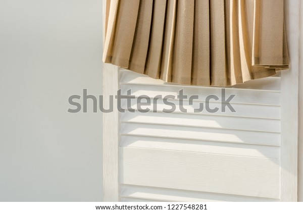 close up of beige pleated skirt hanging on white\
room divider isolated on\
grey
