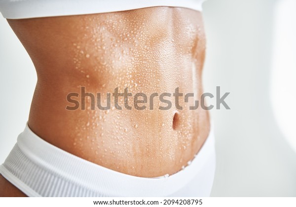 Close up belly of a\
beautiful sporty girl in drop of sweat or water on skin. Body care,\
fitness concept