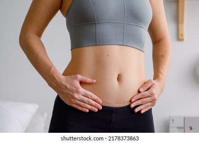 Close up of a belly with scar from c-section. Women's health. A woman dressed up in sportswear demonstrating her imperfect body after a childbirth with nursery on the background.