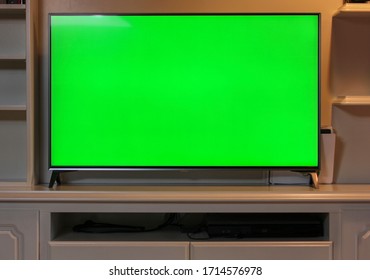 Close Up Of Big Green Screen Led TV In A Cozy Living Room. Modern 55 Inch Sized Television With Chroma Key Green Screen Over A TV Unit.