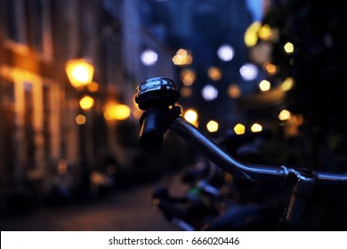 Close up of a bike handle with a bell, shot against nightly city of Leiden filled with city lights, in the Netherlands