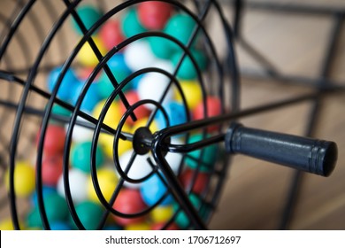 A Close Up Of A Bingo Cage Filled With Multi-colored Balls. Each Ball Has A Letter And Number On It That Corresponds To A Number On The Player's Bingo Card. Bingo Is A Game Of Chance.