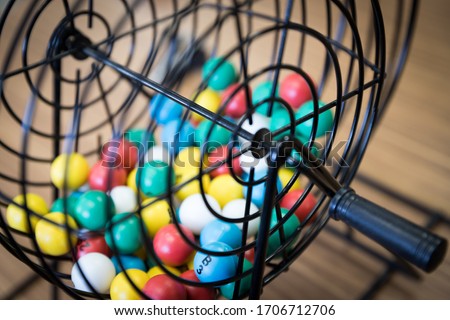 A close up of a bingo cage filled with multi-colored balls. Each ball has a letter and number on it that corresponds to a number on the player's bingo card. Bingo is a game of chance.