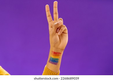 Close up of biracial man showing v sign with lgbt flag on arm on purple background. Lgbt and pride concept. - Powered by Shutterstock