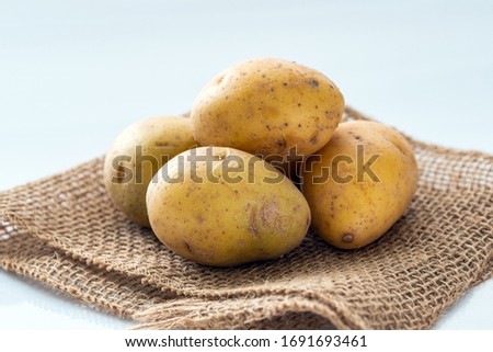 Close up of bite size yellow potatoes on gunny sack, over white background