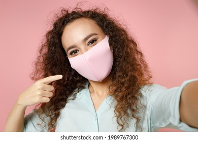 Close Up Black African Woman In Blue Shirt Point Finger On Face Mask From Coronavirus Covid-19 Pandemic Quarantine Doing Selfie Pov On Mobile Phone Isolated On Pastel Pink Background Studio Portrait