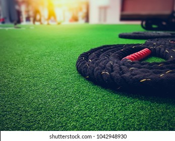 Close up black battle rope for exercise on green grass floor with sunrise in the gym. Copy space