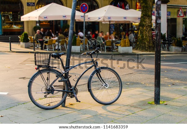 close black bike at\
the post on the city street on the background of the road and\
people in the sun rays.\
