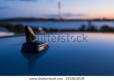 Close up of black car antenna on a roof against bright sunset sky