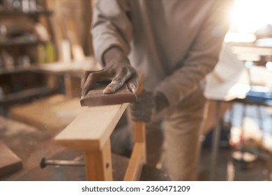 Close up of black craftsman carefully sanding wooden furniture in rustic carpentry workshop, copy space - Powered by Shutterstock