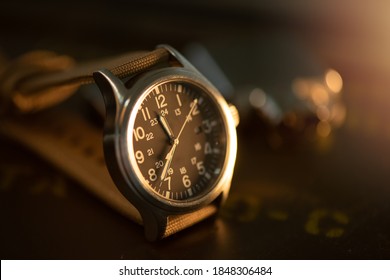 Close up black dial military style wristwatch with biege nylon watch band. Wristwatch for men with military objects in the background. - Powered by Shutterstock