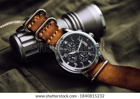 Close up black dial military style wristwatch with black leather watch band. Wristwatch for men with military objects in the background.