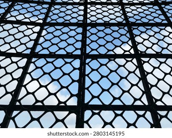 Close Up of Black Diamond Mesh Pattern Against Blue Sky and Cloud Background