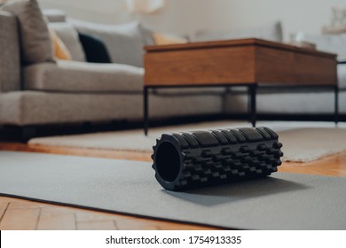 Close up of a black foam roller on a fitness mat, interior of a modern living room, selective shallow focus.