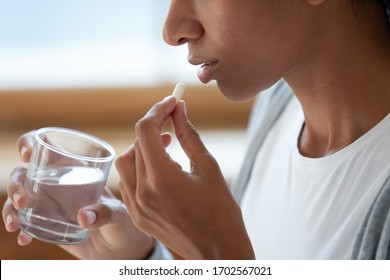 Close up of black girl hold glass of water and white pills at her mouth. Take painkillers, antidepressants, antibiotics, antiviral med. Headaches or menstruation pain. Concept of medicine and pharmacy