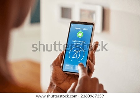 Close up of black hand setting temperature of air conditioner using mobile phone at home. African american woman use smart home app on phone in living room to adjust temperature and ventilation. 