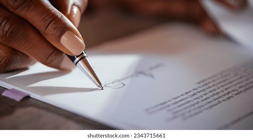 Close up of black hands of businesswoman signing agreement with ballpoint pen. African american hand of a mid adult woman signing a contract. Macro detail of woman signing agreement. 