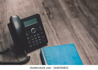 Close Up  Black Ip Phone And Notbook For Call Meeting  Placed On A Wooden Floor In The Office.