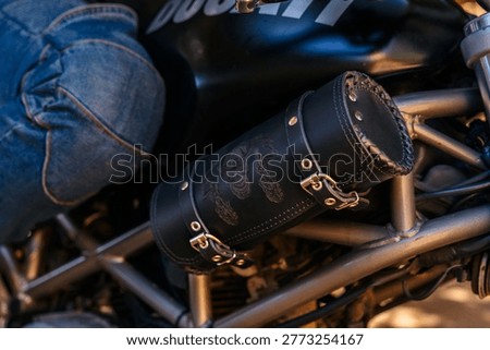 Close up of a black leather tool pouch mounted on a Ducati motorcycle. Visible engraved artwork, metal buckles, and detailed stitching. Warm lighting enhances texture and highlights premium craftsmanship and biker accessory design.