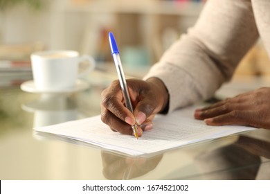 Close up of a black man hands filling out form on a desk at home