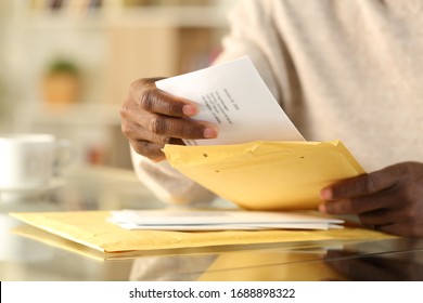 Close up of black man hands opening a padded envelope with letter on a desk at home