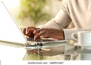 Close up of black man hands typing on a laptop sitting on a desk at home