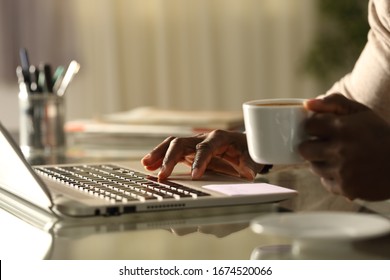 Close up of a black man hands using laptop holding a coffee cup in the night on a desk at home