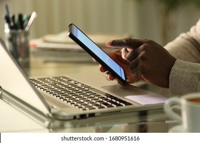 Close up of black man hands using smart phone with laptop on a desk at home