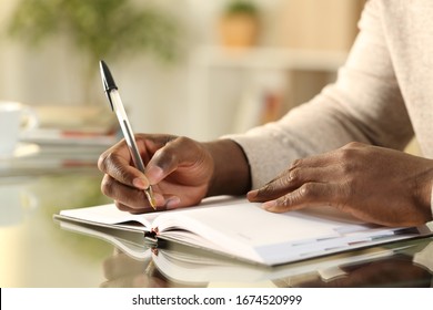 Close up of a black man hands writing reminder on paper agenda on a desk at home