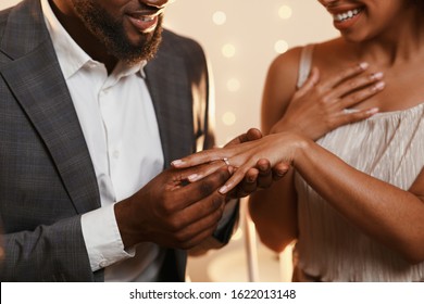 Close up of black man in love putting wedding ring on his woman finger, festive background