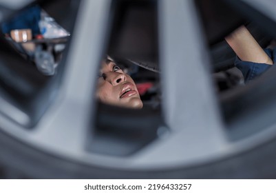 Close Up Black Mechanic Woman Looking Through Car Wheel Working Underneath Car In Auto Repair Shop, Black Female Mechanic Face Concentrate With Car Fixing And Maintenance In Moter Garage