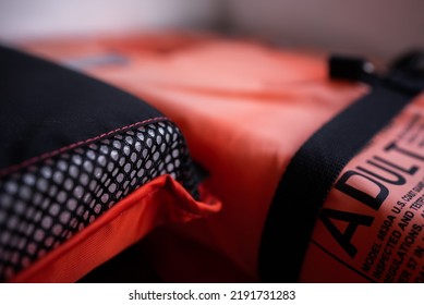 Close up of black netting mesh texture on standard orange life vest for adults aboard white board interior. Type 2 flotation device.
