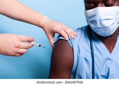 Close Up Of Black Nurse Getting Vaccinated With Syringe And Needle, Wearing Face Mask. African American Medical Assistant Receiving Vaccine Shot From Hands Of Doctor For Virus Protection