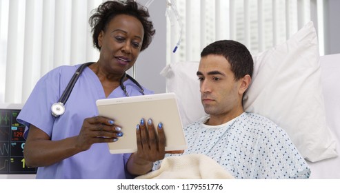 Close Up Of Black Nurse Showing Young Latino Patient Results On Notebook Tablet