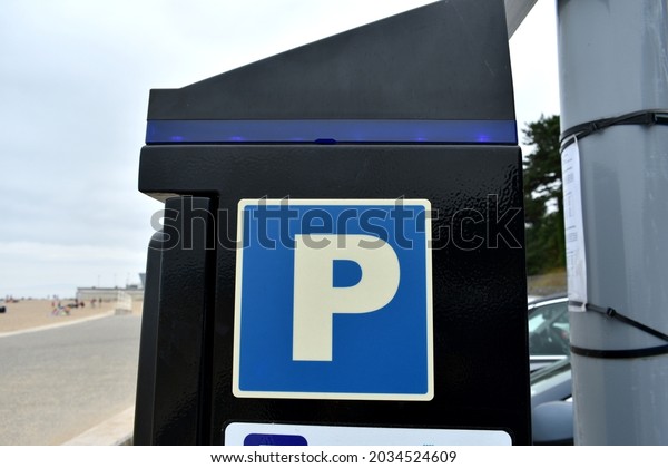 close up of black parking meter box with P\
sign on a pay to car park, on a post outside in summer with coastal\
scene promenade in\
background