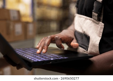 Close up of black person processing orders on laptop and checking inventory, fulfillment center operations for efficient parcel import export for e-commerce retail large business.