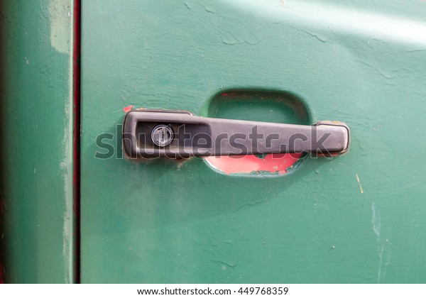 Close up of a\
black plastic car door handle. The vehicle door is green and there\
is red underneath the\
paint.