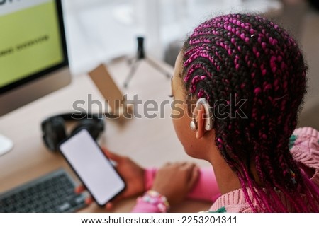 Close up of black teenage girl wearing hearing aid on ear while using smartphone with blank screen at home, copy space