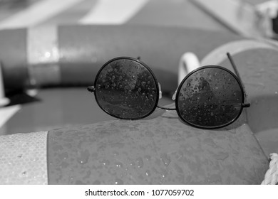 Close Up Black And White Photograph Of Wire Frame Black Sunglasses Covered In Water Droplets On Board A Boat Buoyancy Aid