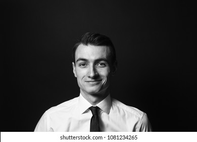 Close Up Black And White Portrait Of A Young Man In A White Shirt And Black Tie, Smiling While Looking At The Camera, Against Plain Studio Background