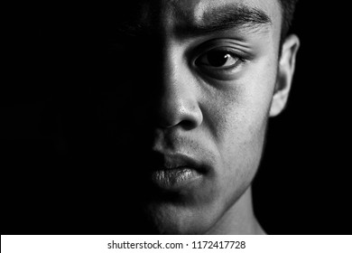 Close up black and white portrait of young male Asian teenager shot in studio using flashlight on black background. - Powered by Shutterstock
