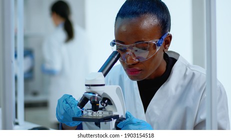 Close Up Of Black Woman Looking In Microscope In Modern Equipped Lab. Multiethnic Team Examining Virus Evolution Using High Tech For Scientific Research Of Treatment Development Against Covid19