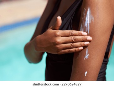 Close up of Black woman spreading sunscreen onto arm with pool background - Powered by Shutterstock