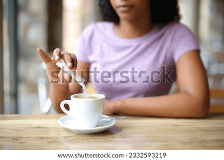 Close up of a black woman throwing sugar in a coffee cup in a bar terrace