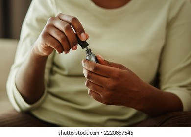 Close up of black young woman holding bottle of silver nail polish while doing manicure at home - Powered by Shutterstock