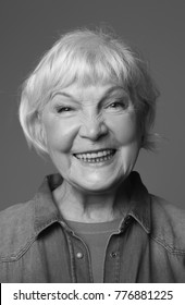 Close Up Black-and-white Portrait Of Mature Lady Smiling While Standing. Isolated On Grey Background