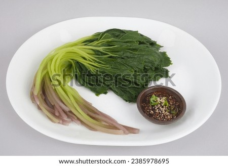 Close up of blanched butterbur leaf and stem on white dish with seasoned soy sauce on small bowl, South Korea
