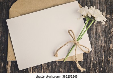 Close Up Of Blank White Greeting Card With Brown Envelope And Wither Mum Flowers On Wooden Table With Vintage And Vignette Tone