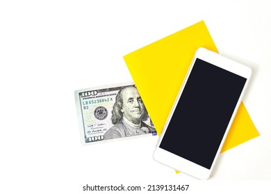 Close Up Blank Yellow Piece Of Paper, 100 Dollar Bill And Empty Screen Mobile Phone On Blue Background